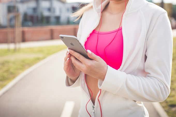 Foto de una mujer del cuello para abajo usando audífonos con cable rojo y sosteniendo un iPhone