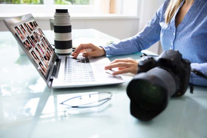 Una mujer sentada en una computadora portátil Mac, trabajando en fotos con la cámara a su lado